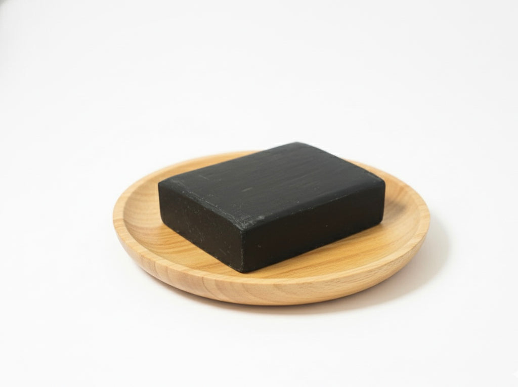 Black soap bar on a wooden plate with a white background