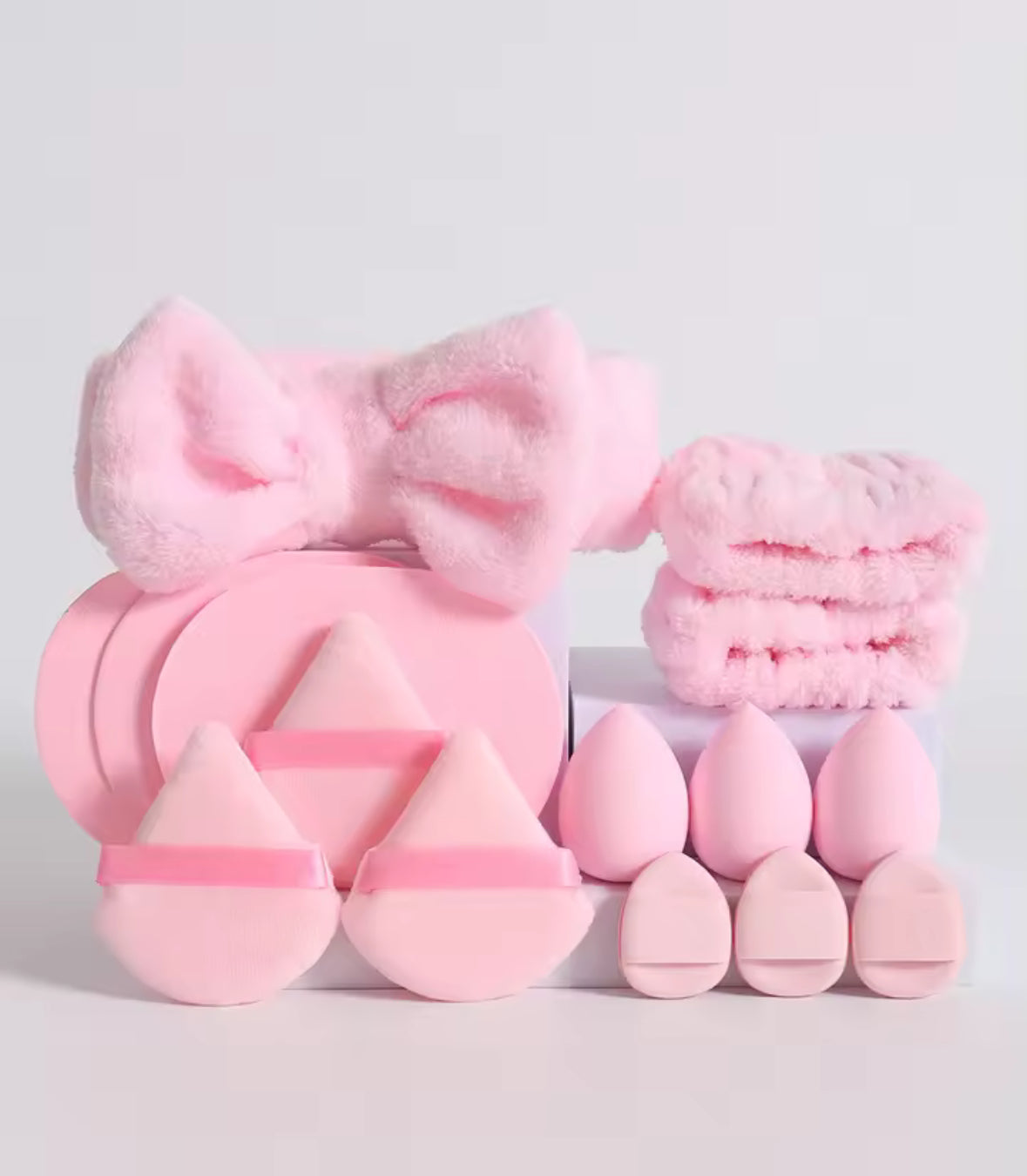 Set of pink beauty tools including a brush, sponges, and a bow on a light gray background