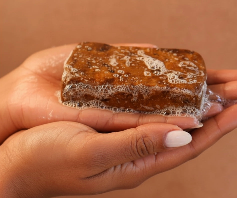 Hand holding a African black  bar of soap with bubbles against a beige background